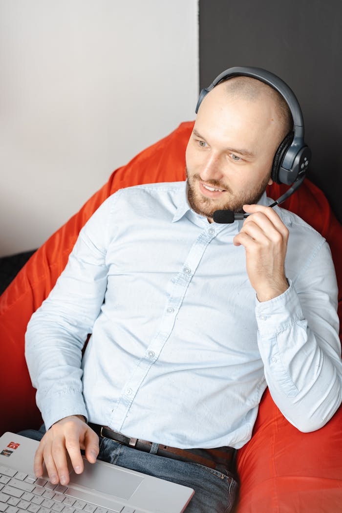 Professional man in blue shirt using headset and laptop from home office.